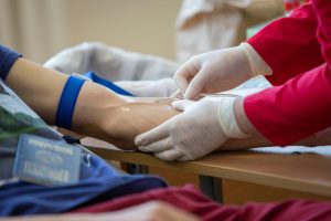 medical professional inserting needle into patient’s arm to draw blood